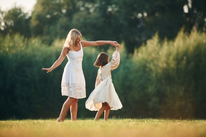 A woman dances with a young girl in a field.