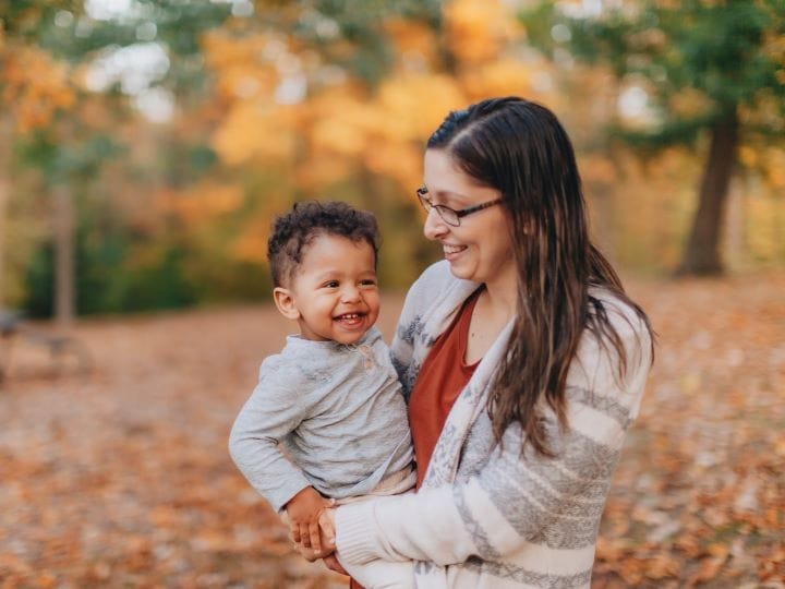 A woman smiles at a child she holds in her arms.